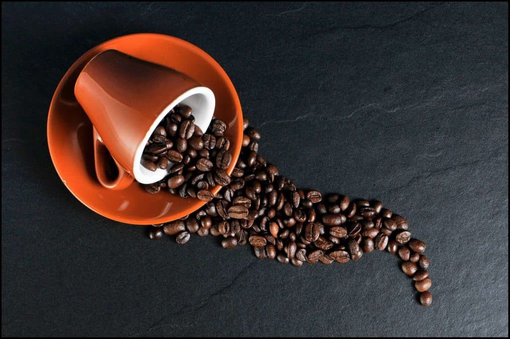 Café com blockchain: desvendando o caminho do grão à taça de café. Imagem com fundo preto, caneca vermelha derramando grãos de café na superfície.